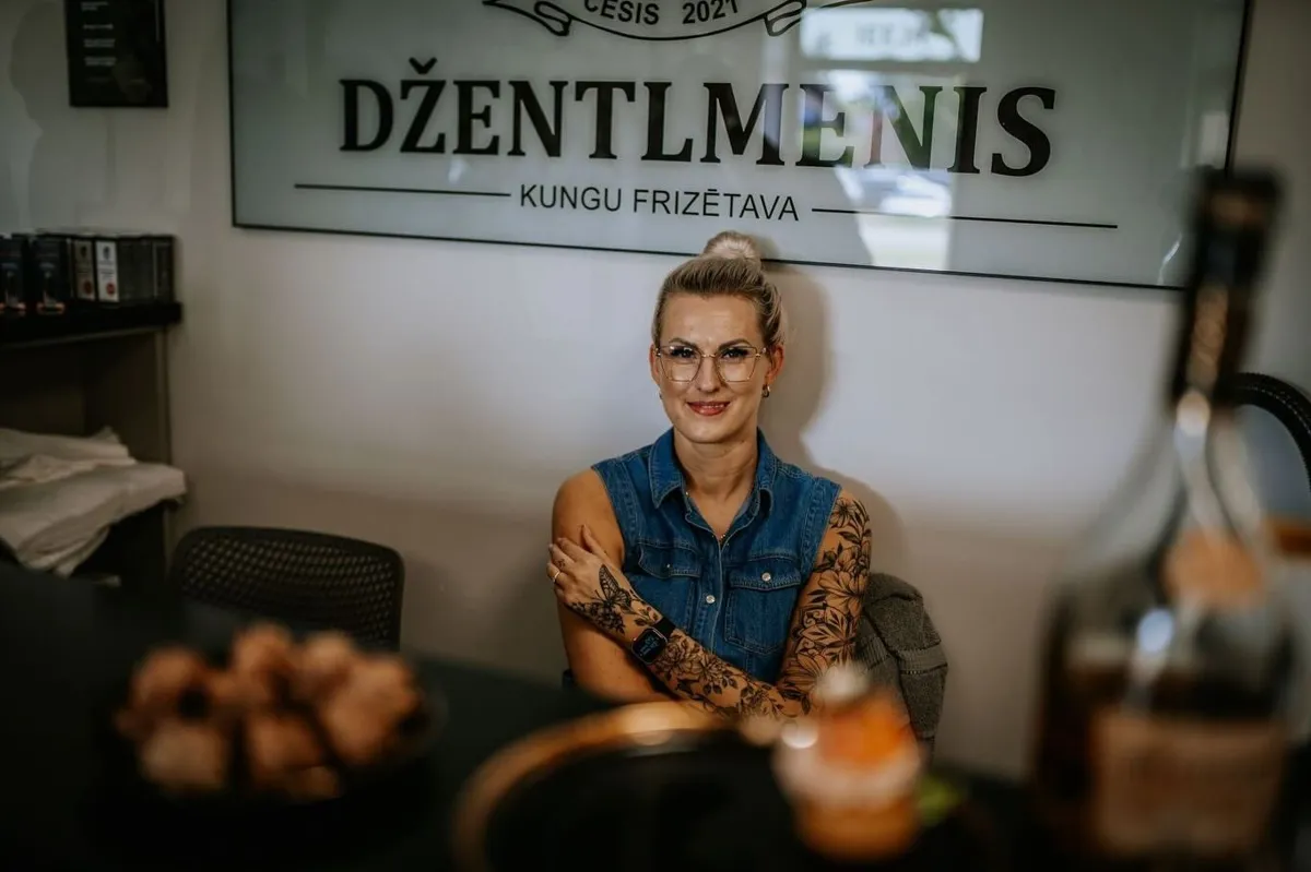 Izkārtne „DŽENTLMENIS – kungu frizētava” pie salona sienas, zem tās frizieris