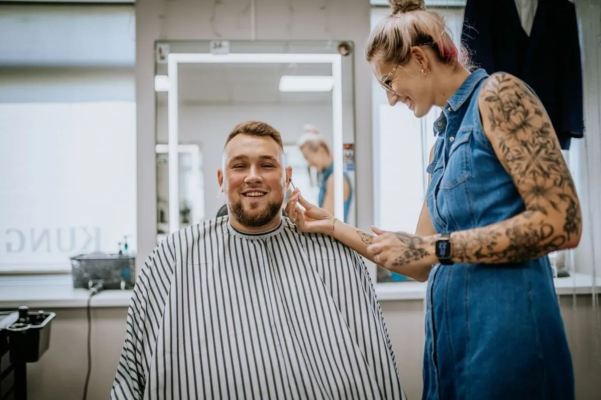 Frizieris DŽENTLMENIS salonā pie smaidoša klienta ar koptu bārdu