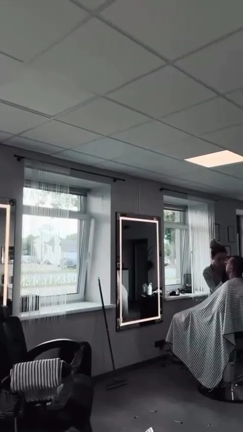 Salona telpa ar logiem, gaismas spoguli un klientu frizieru krēslā