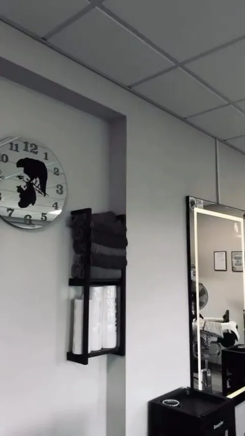 Pulkstenis ar DŽENTLMENIS logo siluetu un dvieļu plaukts salonā